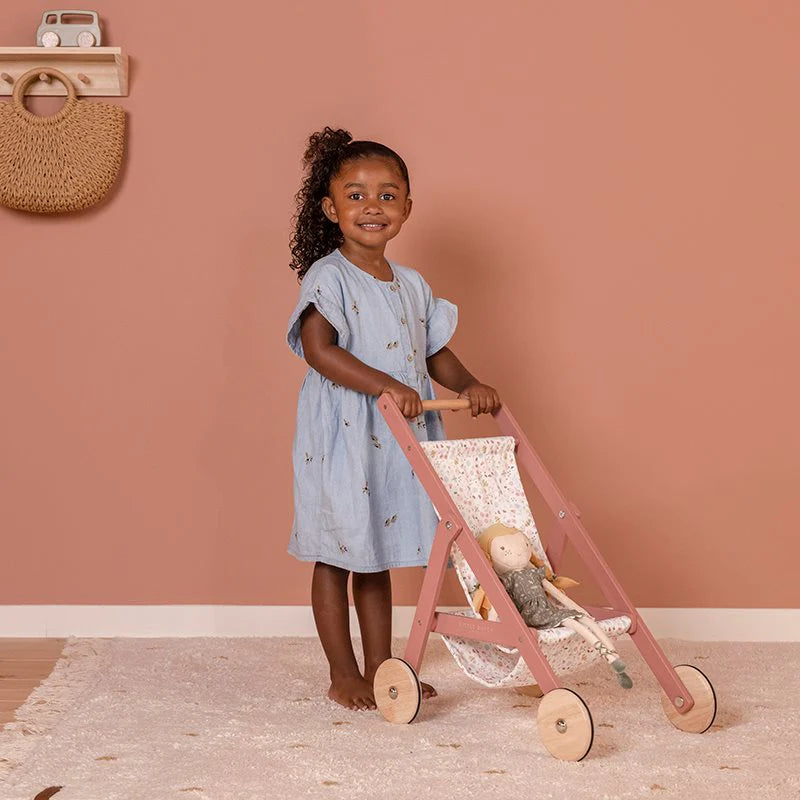 A little girl pushing the Little Dutch pushchair with a doll in with a pink background