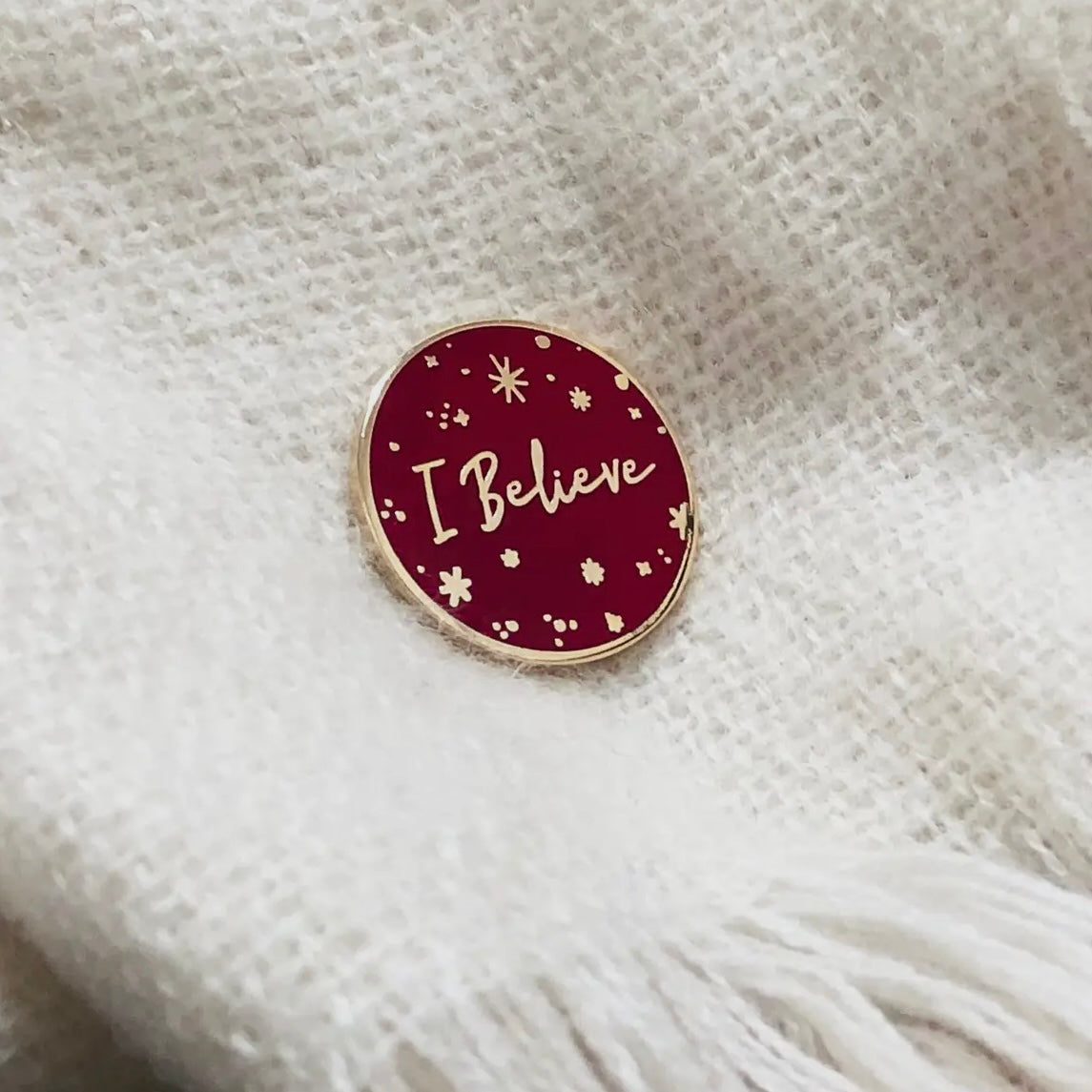 A red and gold pin badge with the words I believe on