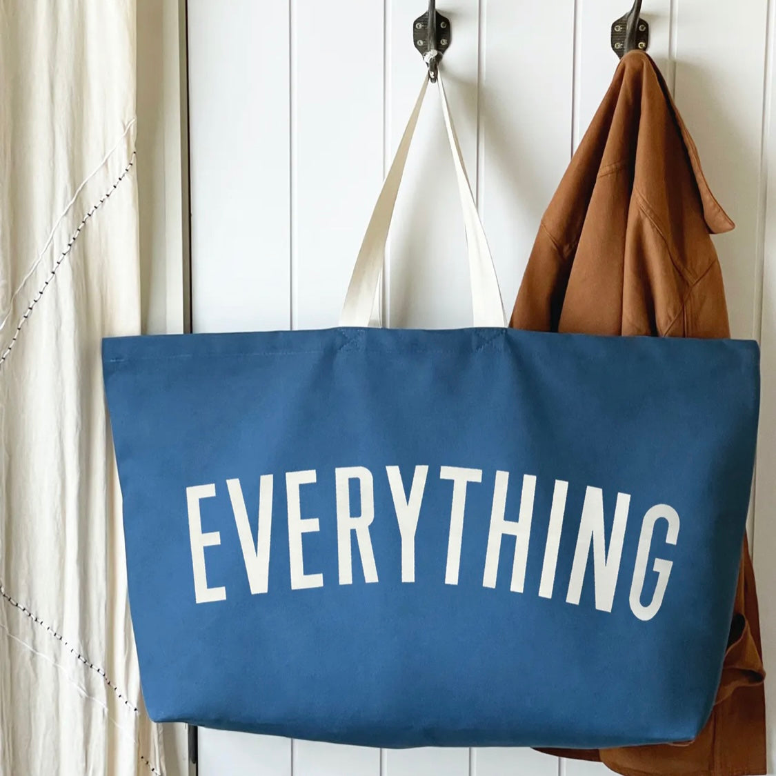 large blue tote bag screenprinted with the word everything in white on a peg