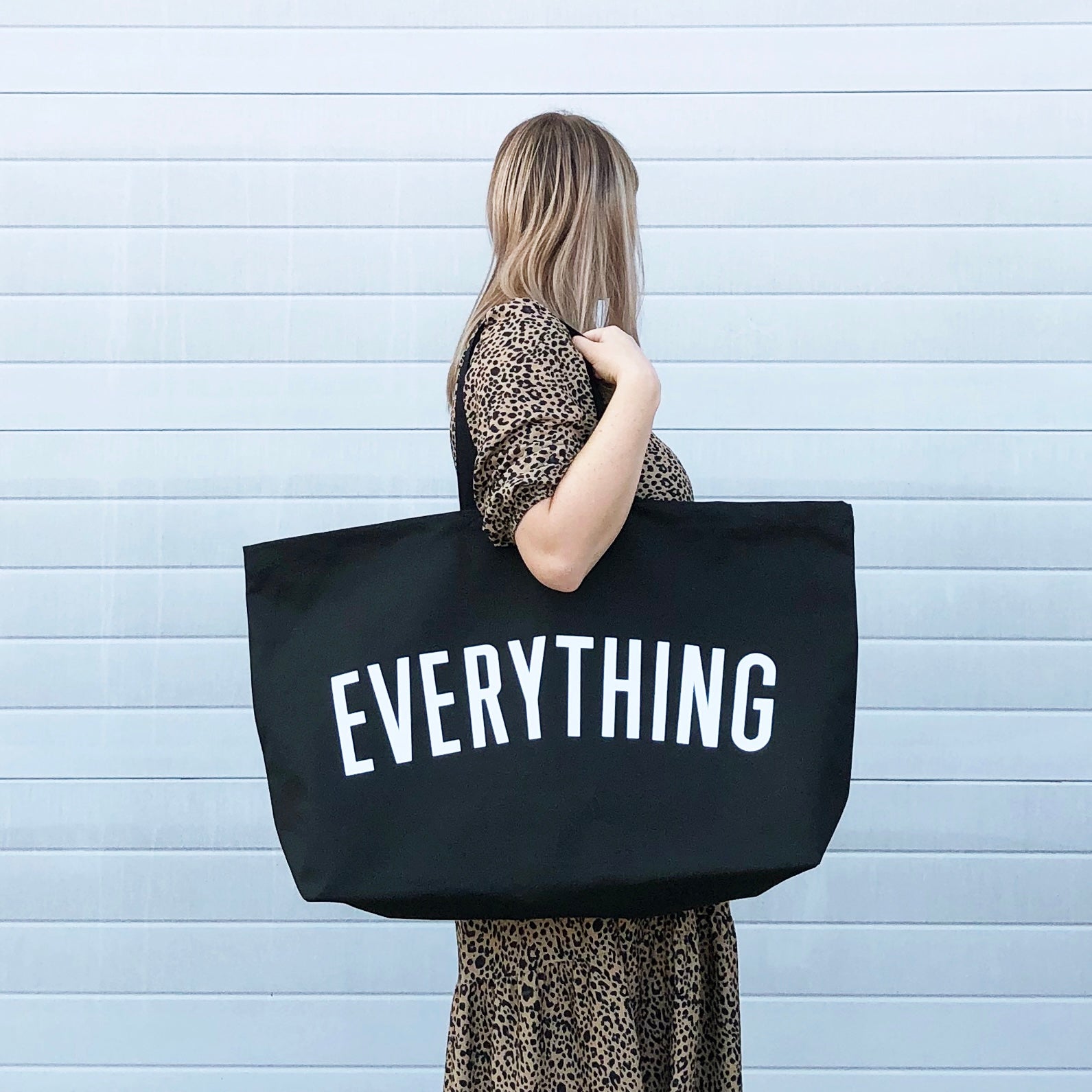 a person holding a large black tote bag with the word everything screenprinted in white
