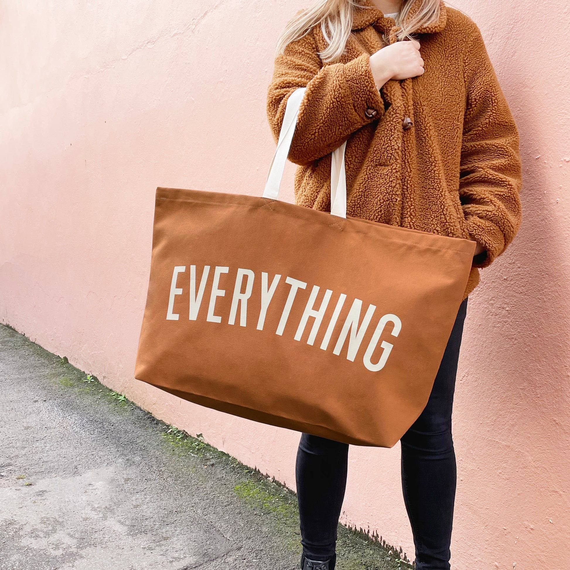 person holding a tan coloured canvas tote bag screenprinted with the word everything