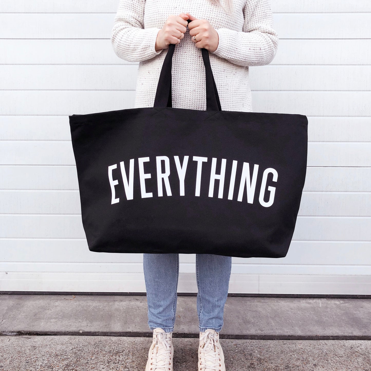 a person holding a large black tote bag with the word everything screenprinted in white