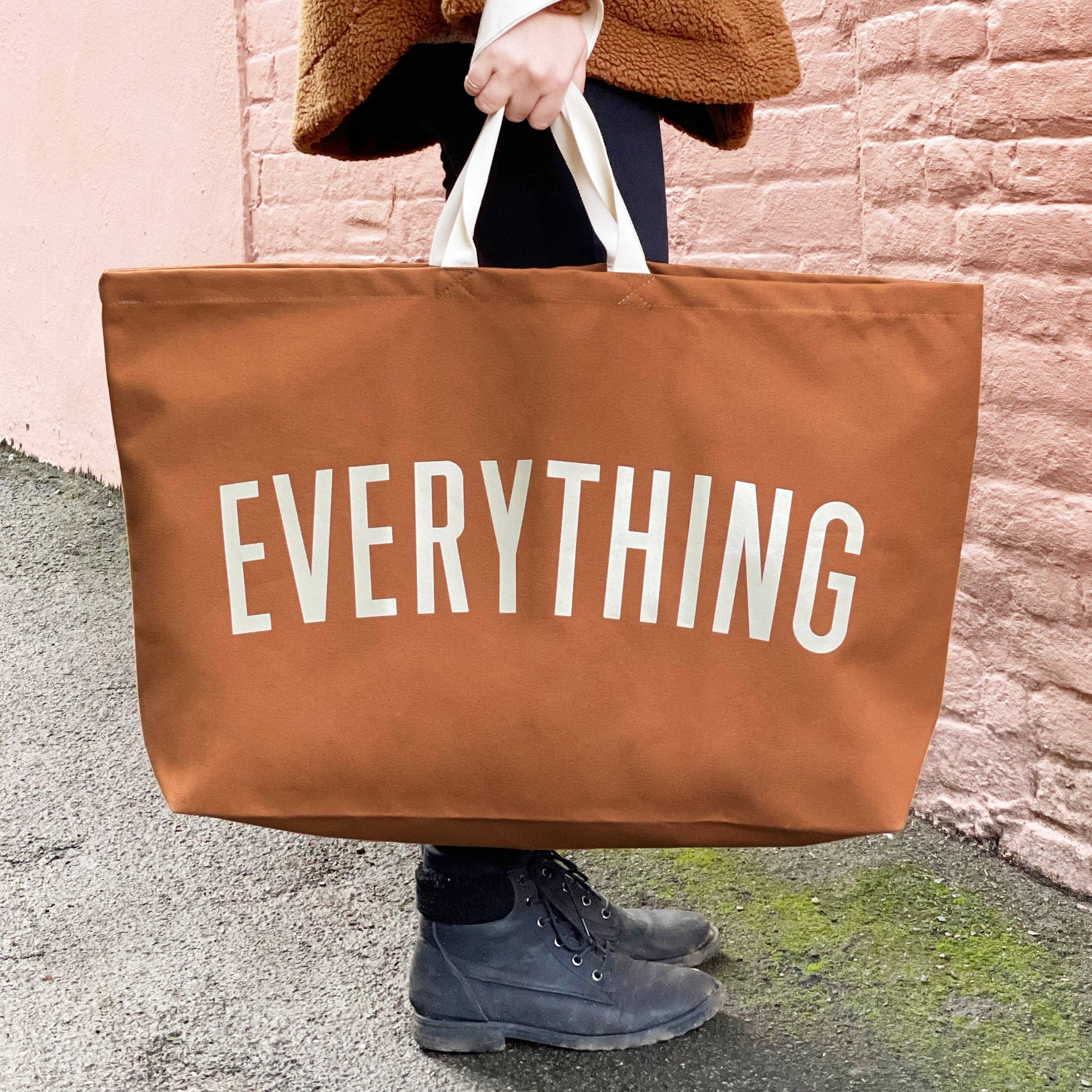 person holding a tan canvas tote bag screenprinted with the word everything