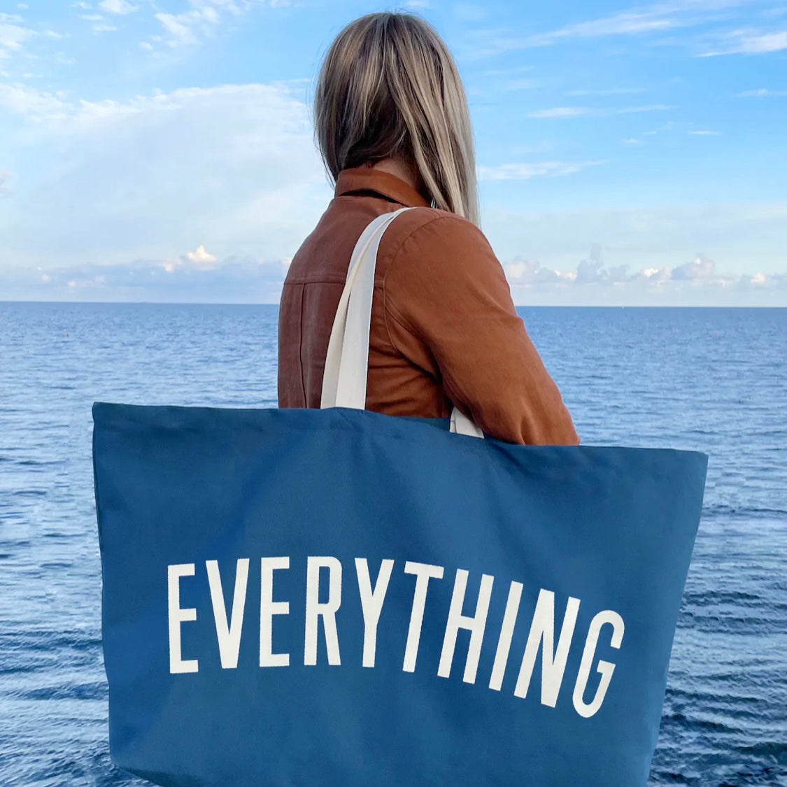 person holding a large blue tote bag screenprinted with the word everything in white